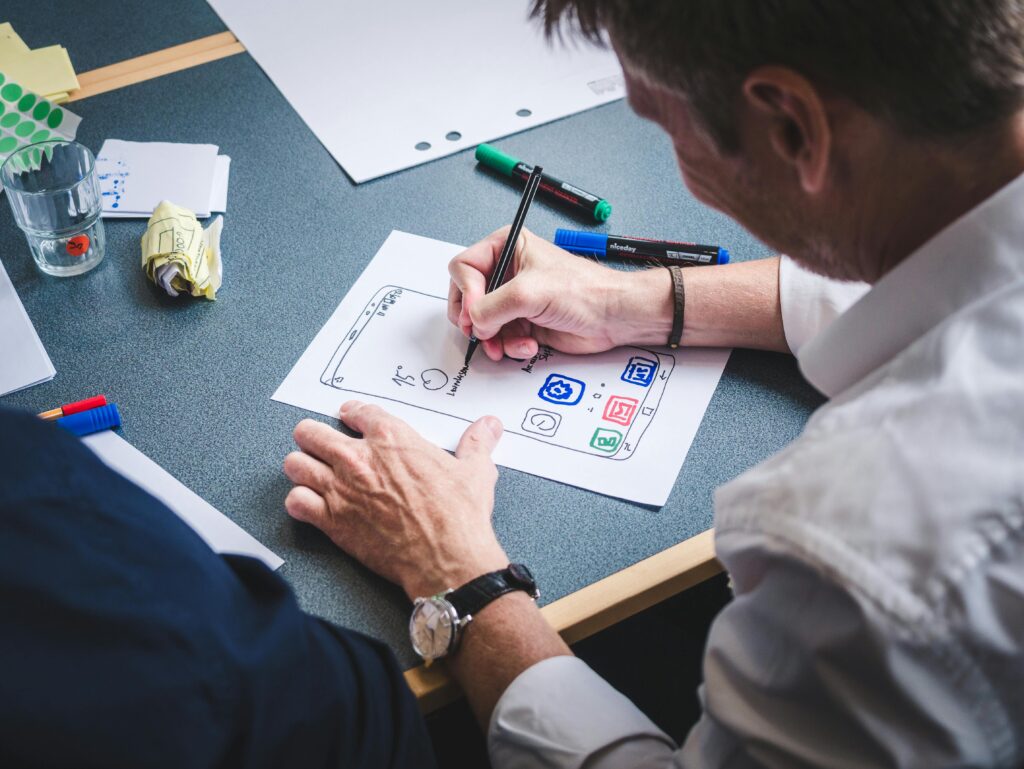 pexels photo 3471423 3471423 A designer sketches a mobile app prototype on paper at an office desk, focusing on creativity and design.